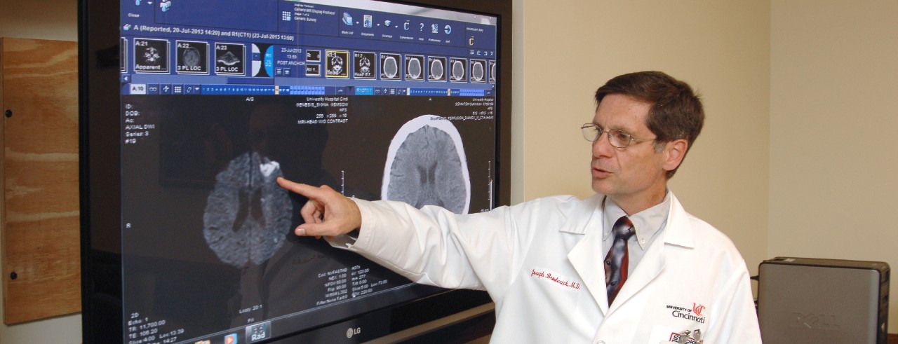 Dr. Broderick, wearing a white coat, points at X-rays on a screen