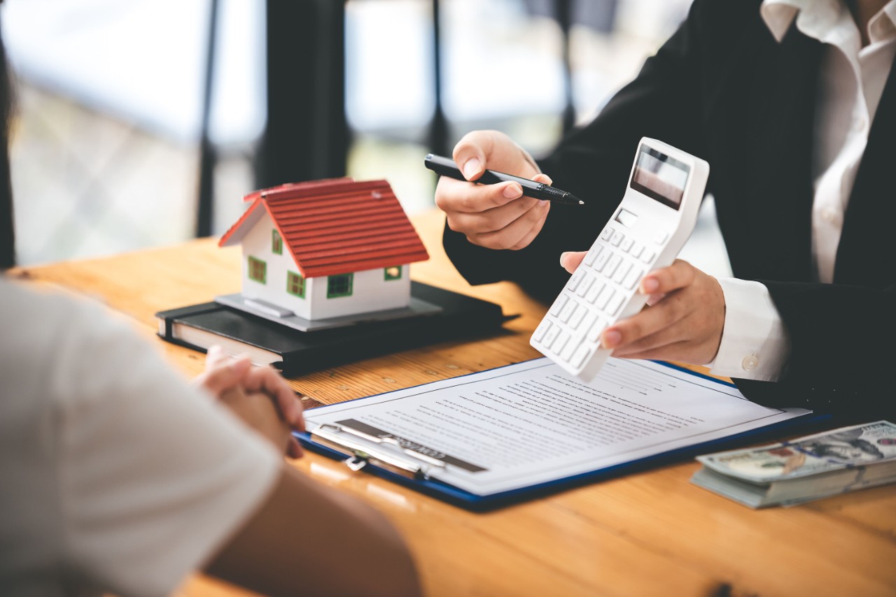 A stock image of a person holding a calculator above paperwork with another person sitting across the table.