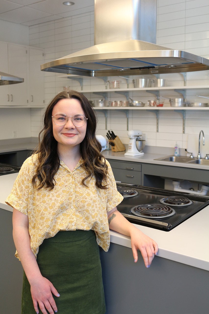 Adeline stands in front of a counter with stovetops and stand mixers in the Foods Lab