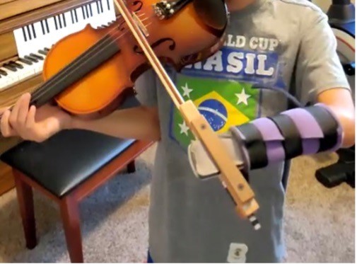 Child using violin bow holder developed by UC students with May We Help
