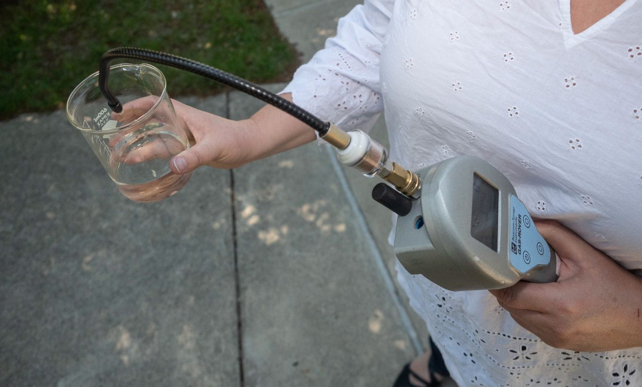 A handheld device measures chemicals in a beaker of water.