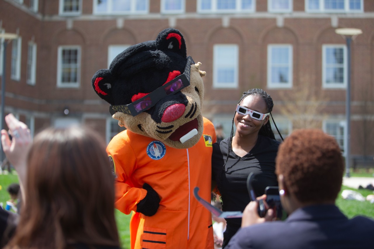 Bearcat mascot wear sun glasses and students next to several students including one young woman with glass to watch the 2024 solar eclipse