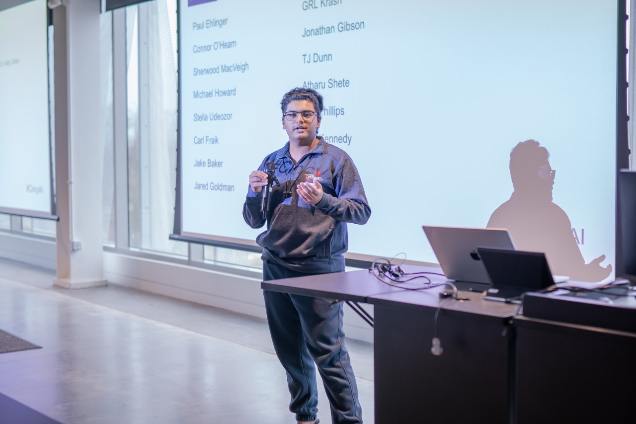 Atharv Shete holds a microphone and speaks to a room full of people.