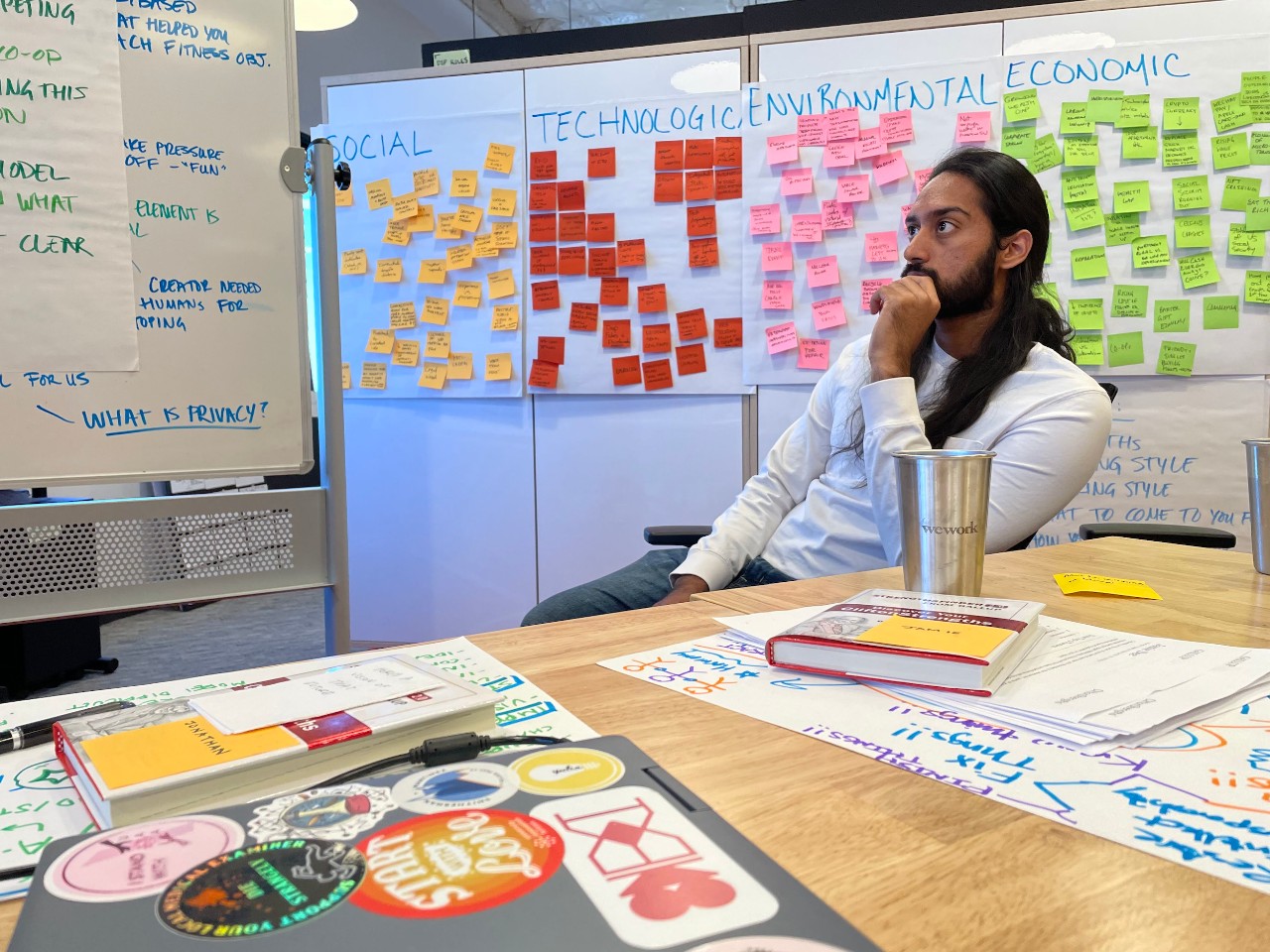 UC student Jonathan Raj sitting in classroom with whiteboards covered in sticky notes in backgroound.