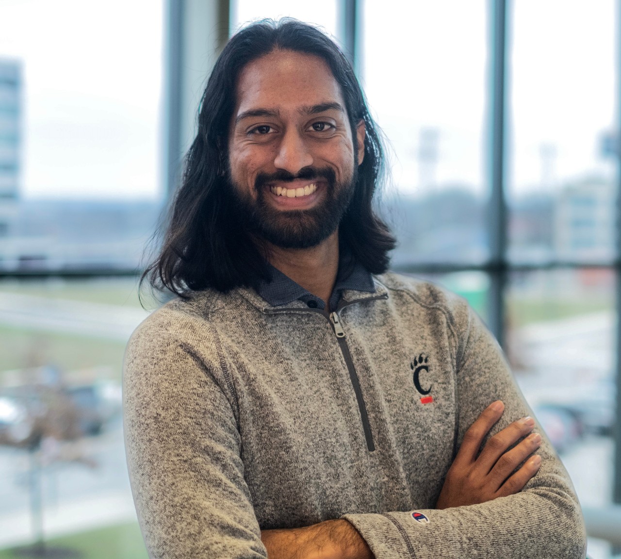Portrait photo of UC student Jonathan Raj with building windows in background.