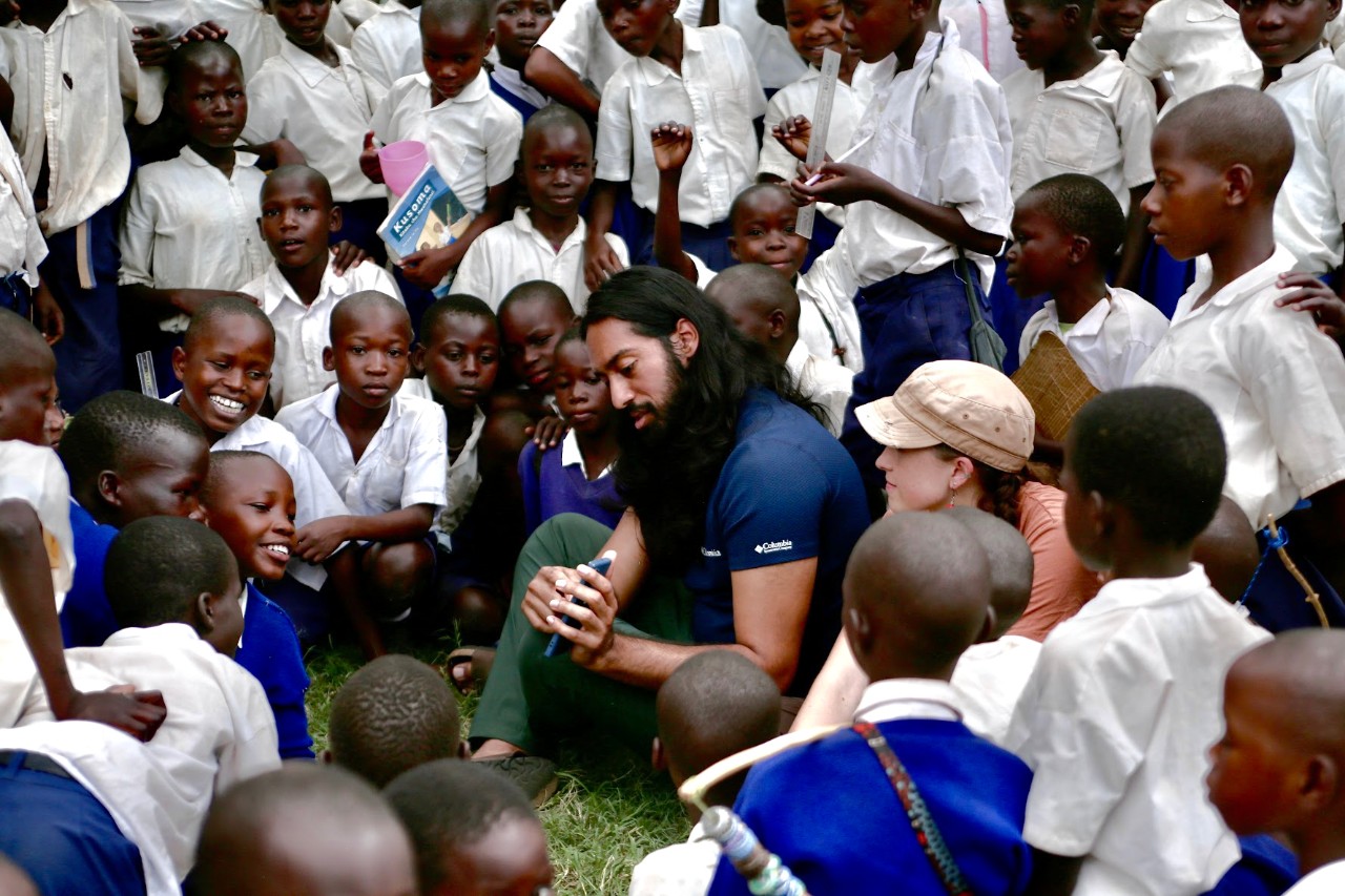 UC student Jonathan Raj sits in the center holding his cell phone while surrounded by dozens of Tanzanian school children.