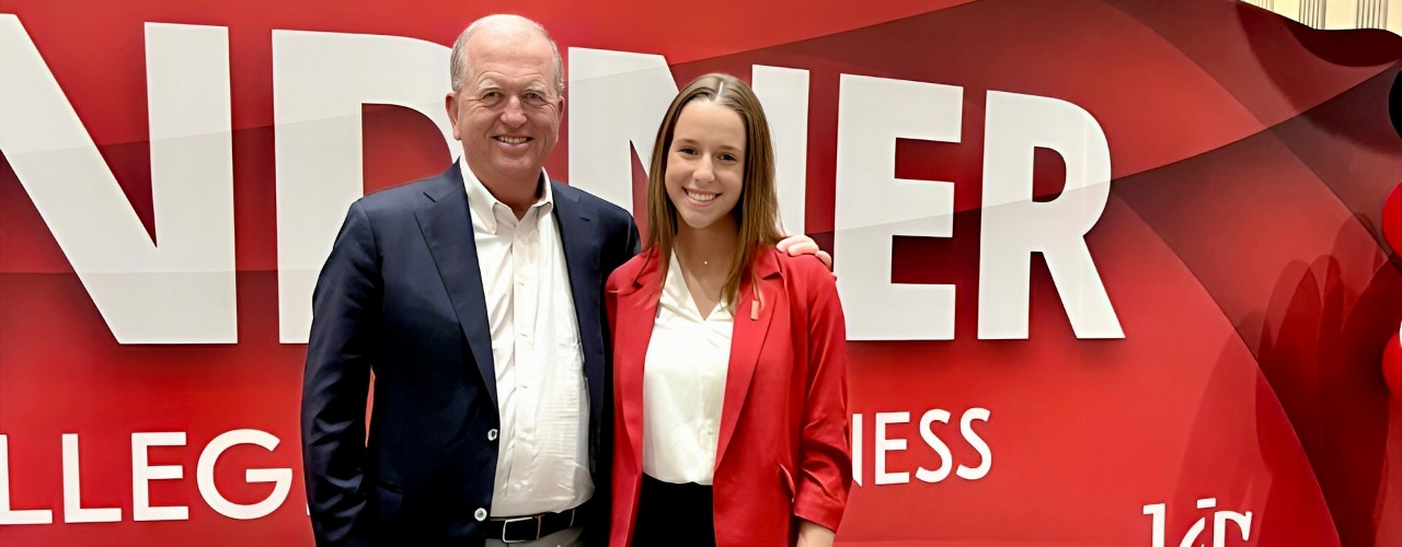 UC business student stands on the right next to Robert King on left in front of a Lindner College of Business wall sign.