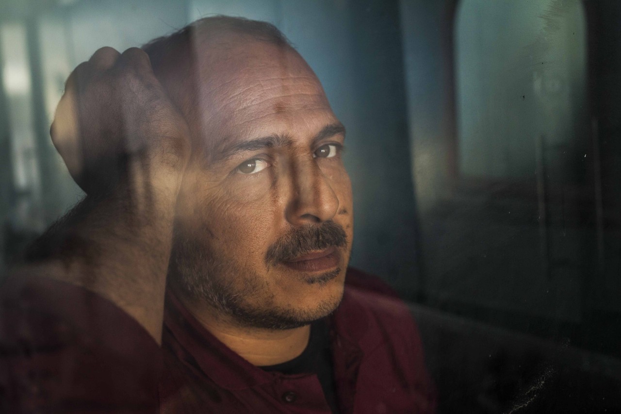 A man with a mustache rests his elbow and face on a window with his head on the back of his head