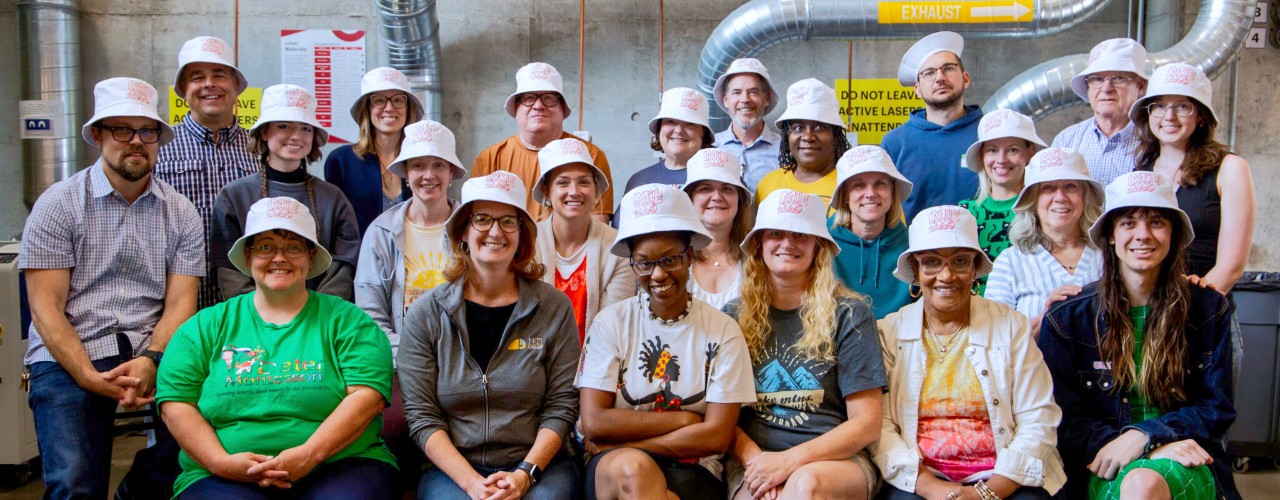 Several men and women wearing white hats sit and stand together facing forward.