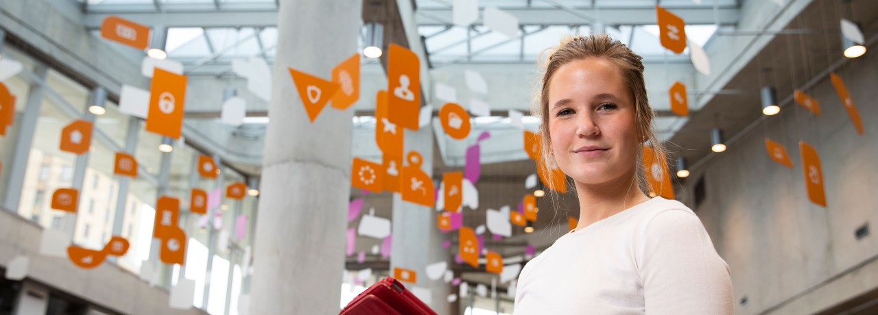 female standing with red ipad wearing white shirt and there are flags hanging from the ceiling above her