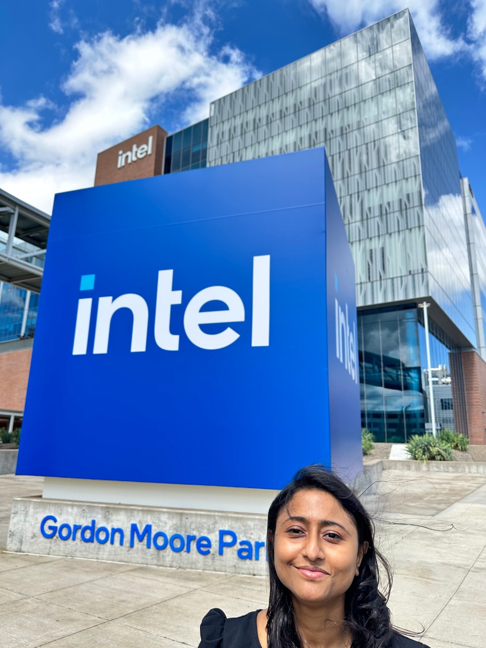 A woman stands in front of a large blue Intel building. 