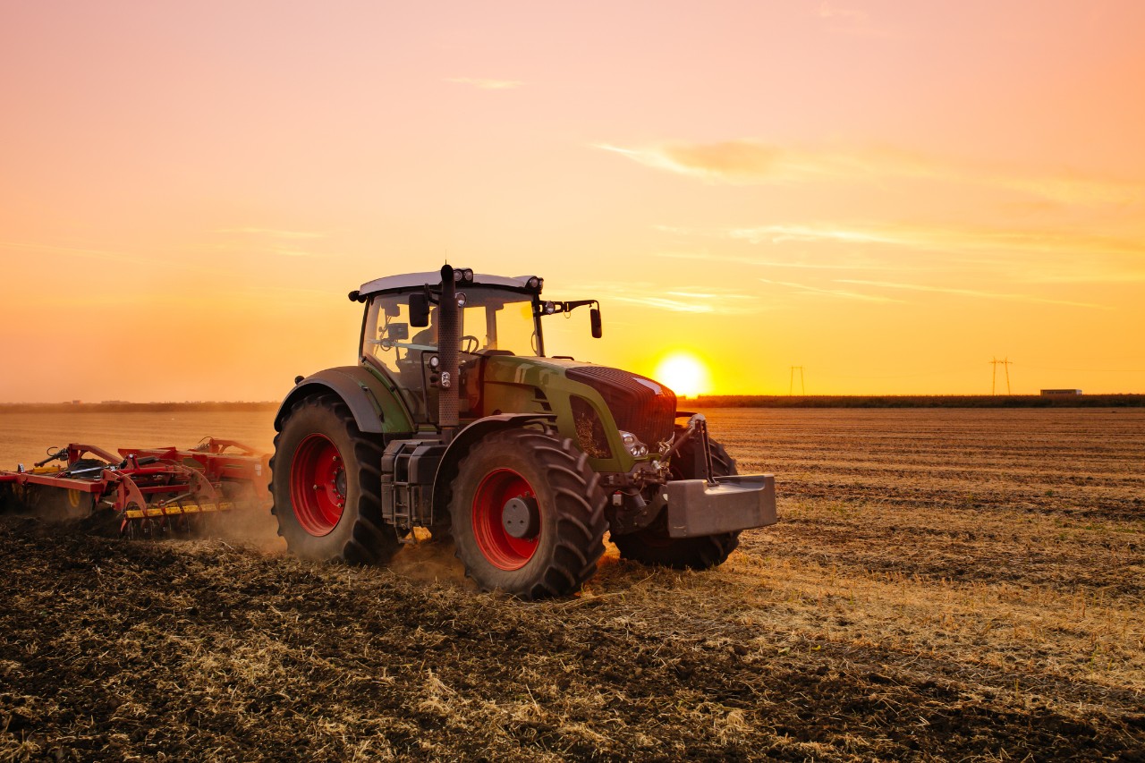 A tractor tills up the soil as the sun rises behind it.