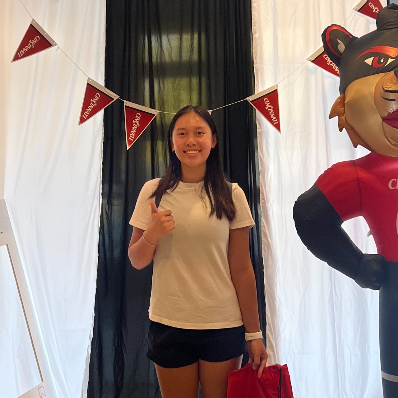 Leia Han stands in front of a black curtain with a thumbs up. There is a UC banner behind her. 