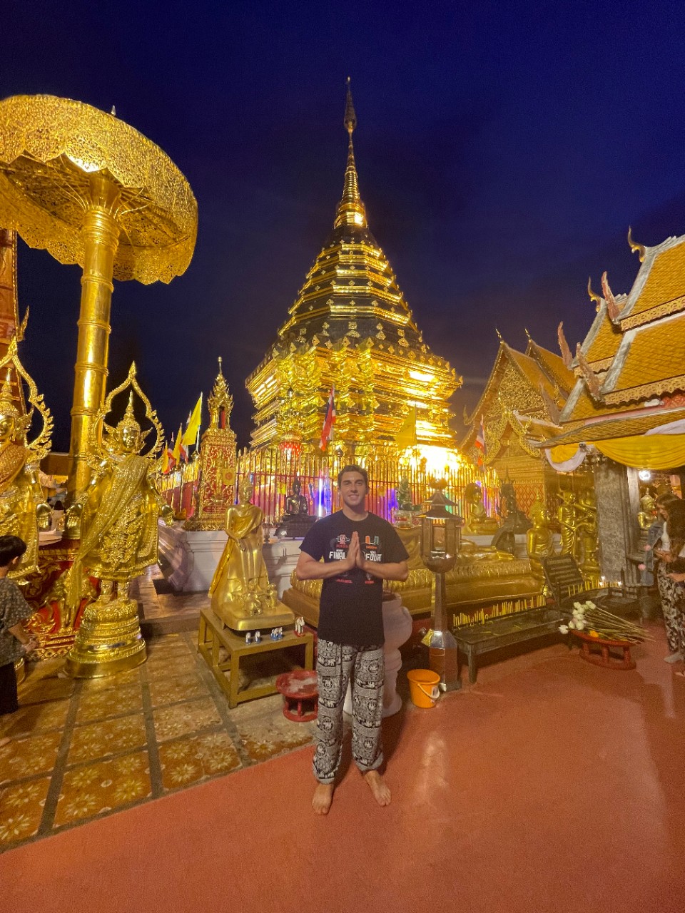 UC student Alex Draginoff poses in front of a temple with his hands in a prayer pose.
