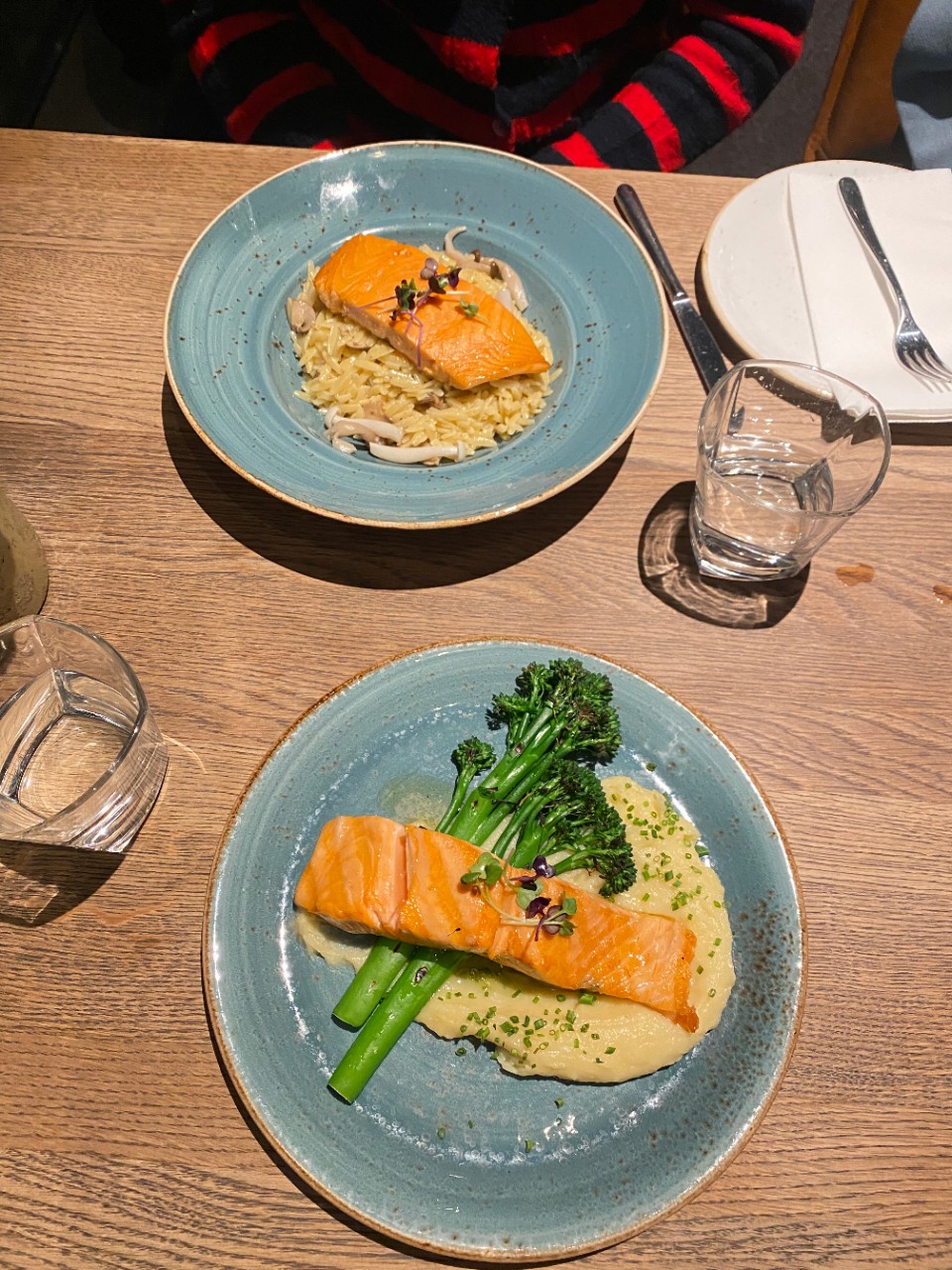 Two plates on a table with two pieces of salmon and broccoli.