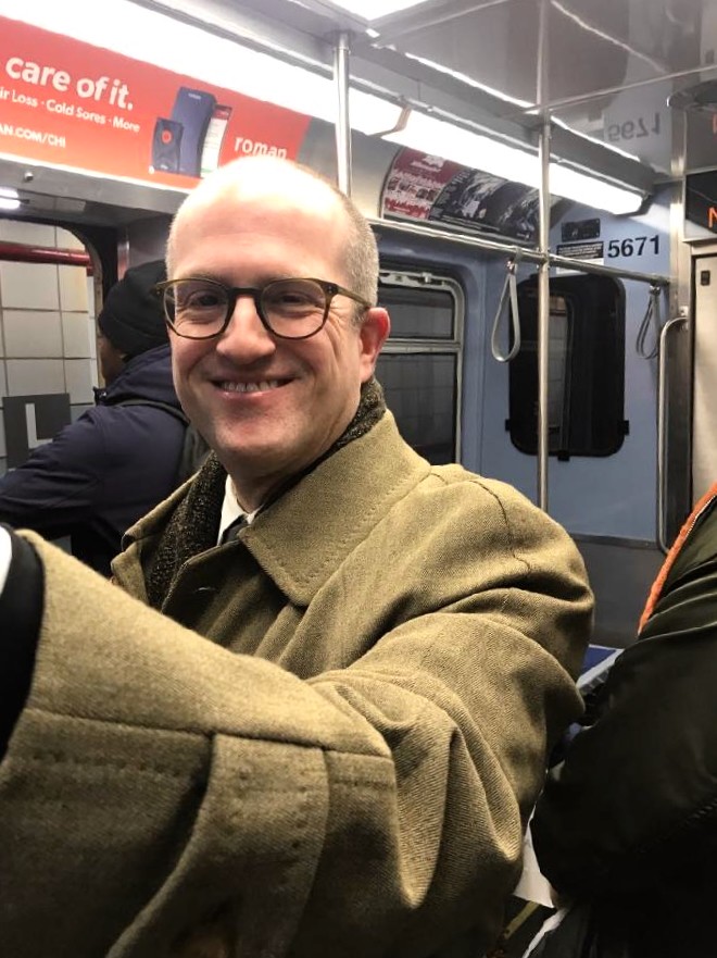 Man facing forward holds onto a pole inside a Chicago 'L' train line car.