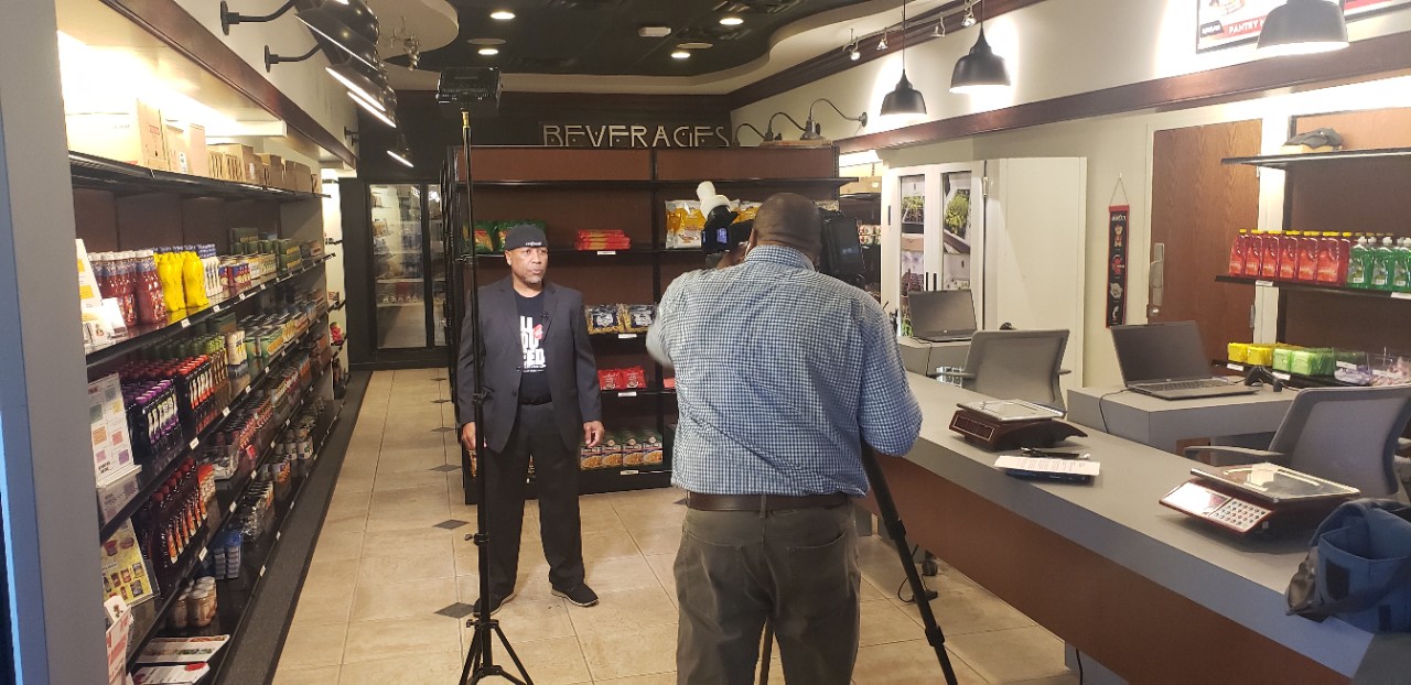 Daniel Cummins stands in the Bearcats Pantry while TV journalist Jason Maxwell trains a camera his way