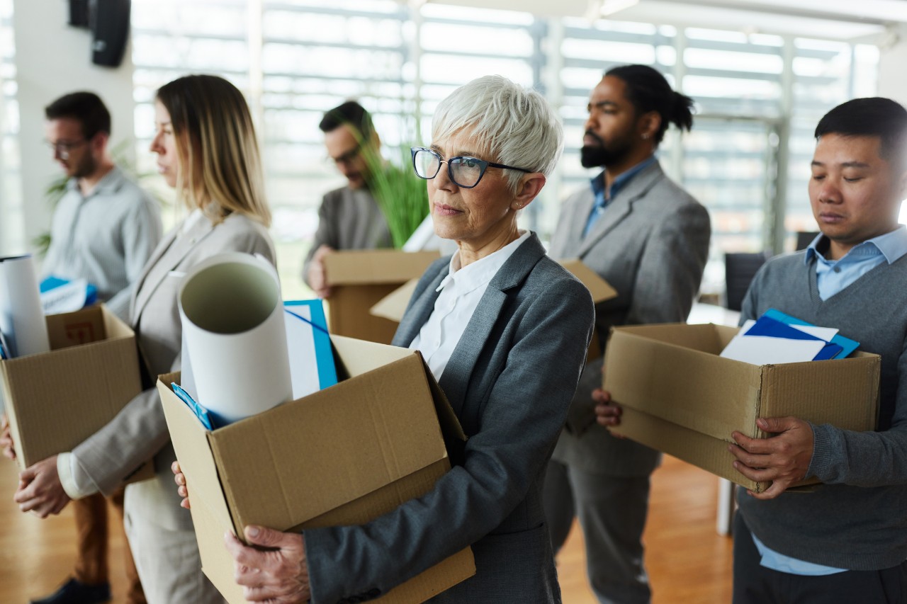 image of several people carrying boxes and leaving an office after being fired