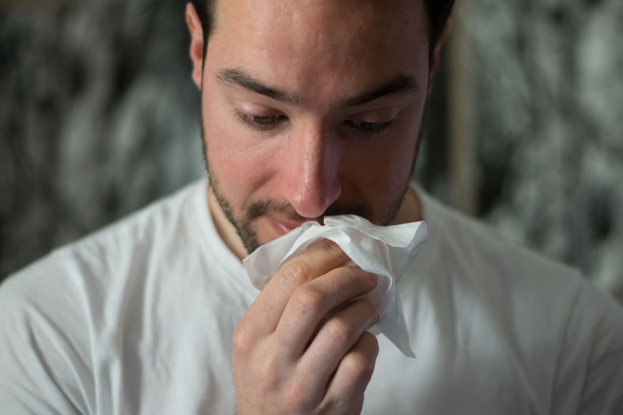 A man sneezes into a white tissue.