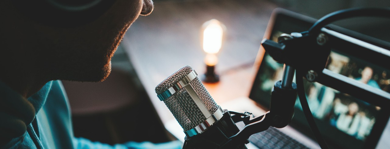 person with a microphone looks at a laptop screen while hosting a podcast