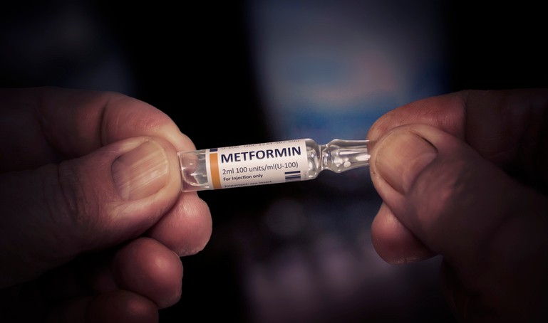 A pair of hands holds a vial labeled "Metformin"