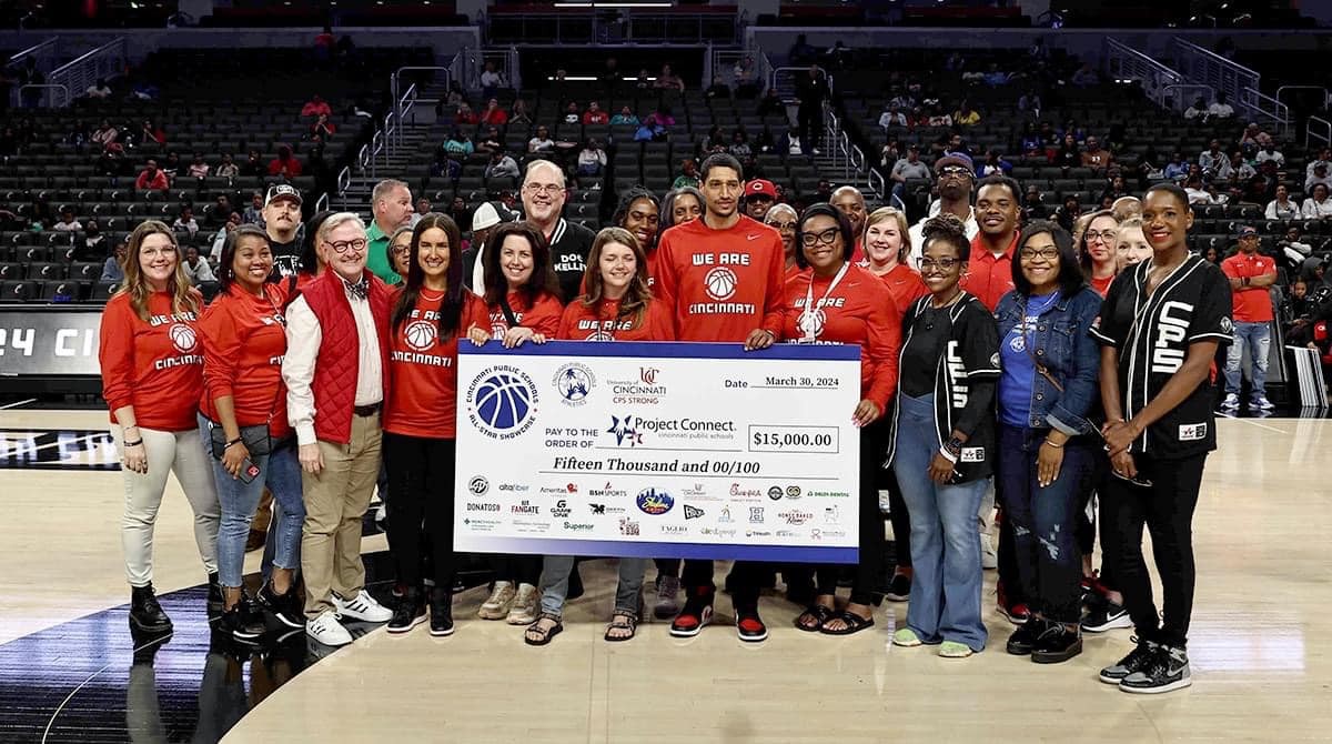 More than three dozen people, Cincinnati Public Schools officials and UC officials, stand behind a poster board check showing $15,000 raised