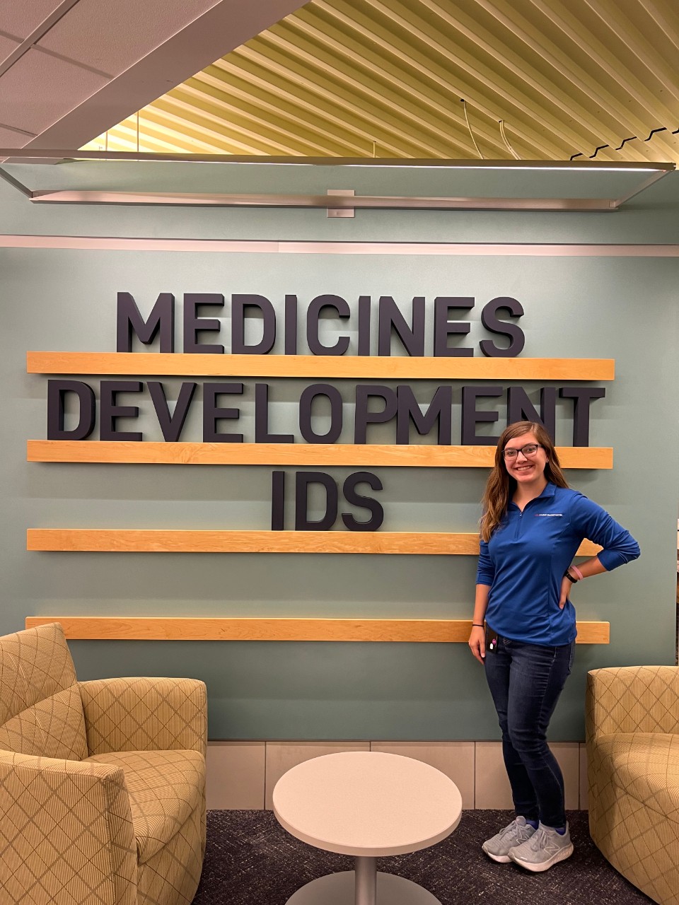Teresa Hawk stands in front of a wall sign that reads 'medicines development IDS'