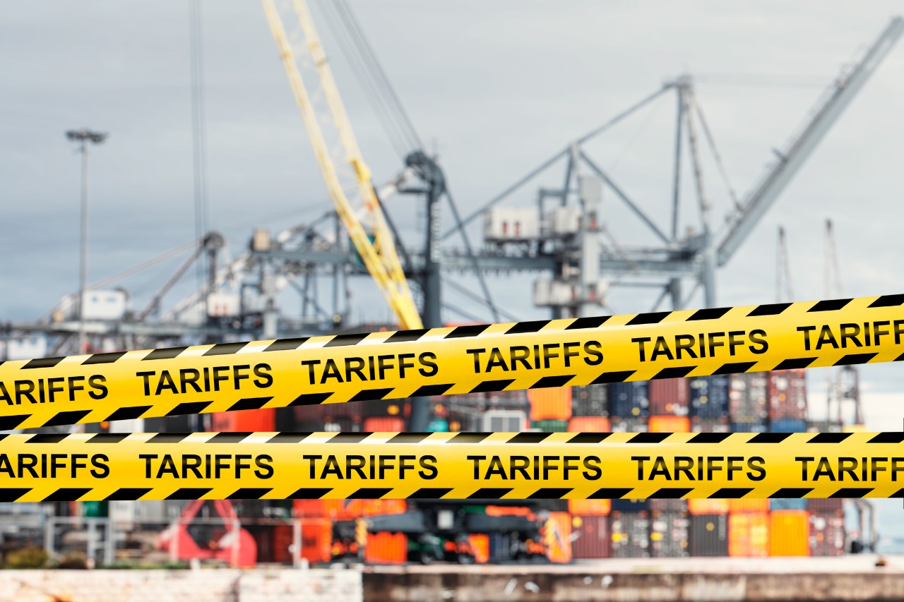 Caution tape reading "tariffs" over shipping containers