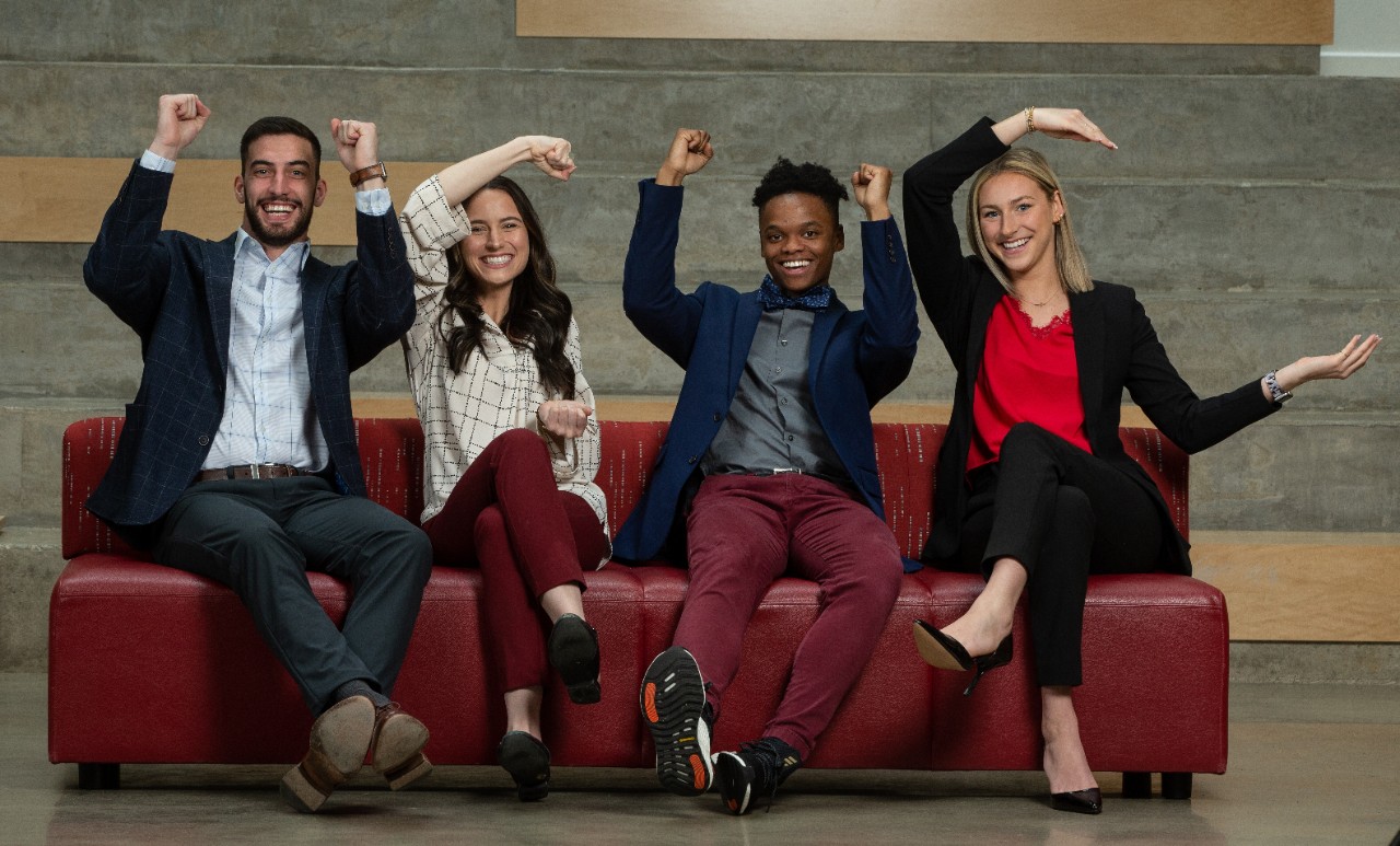 UC co-op students sit on a couch together creating the UC symbol with their arms