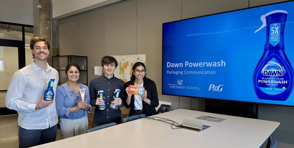 four young people pose next to a presentation screen