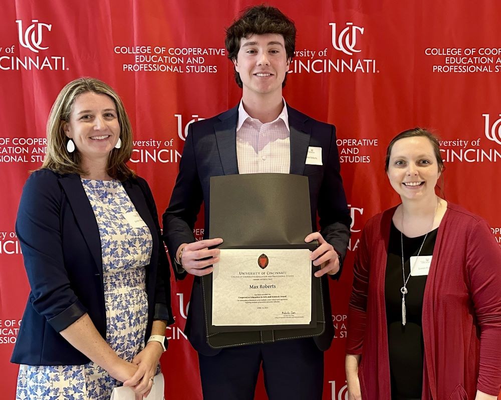 young man with awards certificate stands between two faculty members