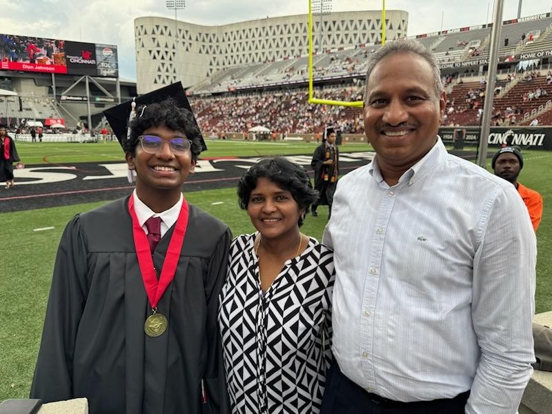 Sai Gollamudi, dressed in graduation cap and gown, is shown with his parents on Nippert Stadium field.