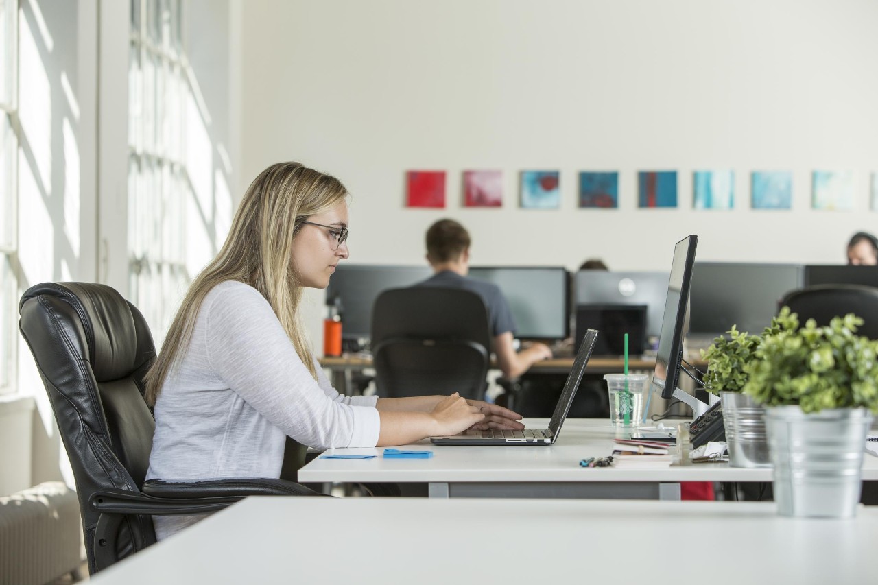 Side profile of young woman at desk on laptop, looking for an entry-level tech job