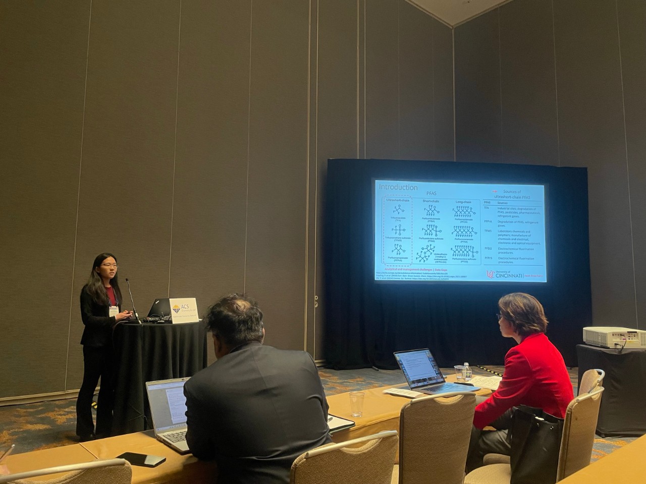 Karen Noda Morishita stands at a podium and gives a presentation on PFAS. 