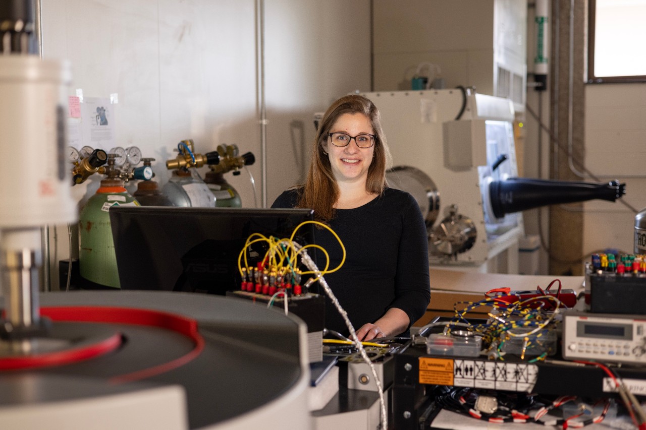 Sarah Watzman stands behind her computer in her lab with equipment surrounding her 