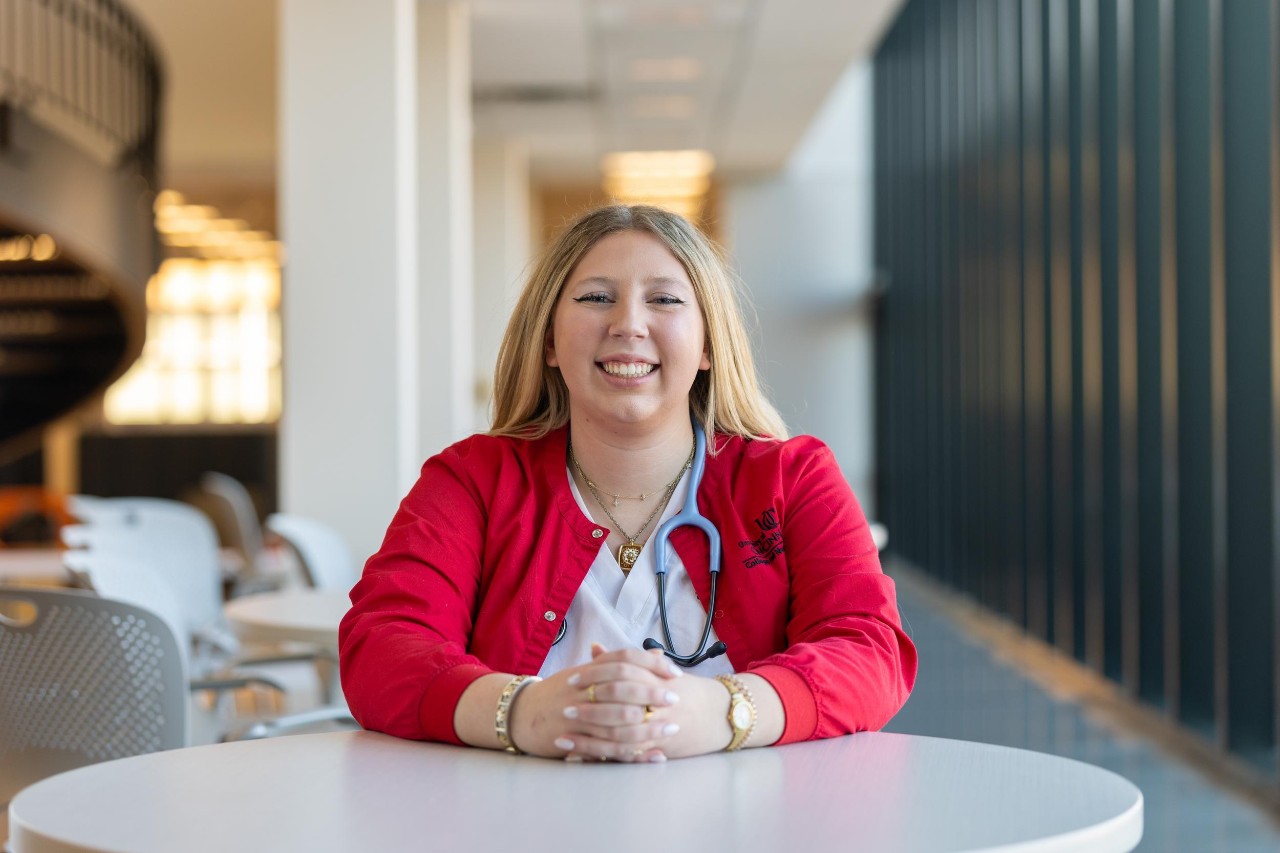 UC Nursing Student Elisse Martin shown in scrubs seated in the College of Nursing