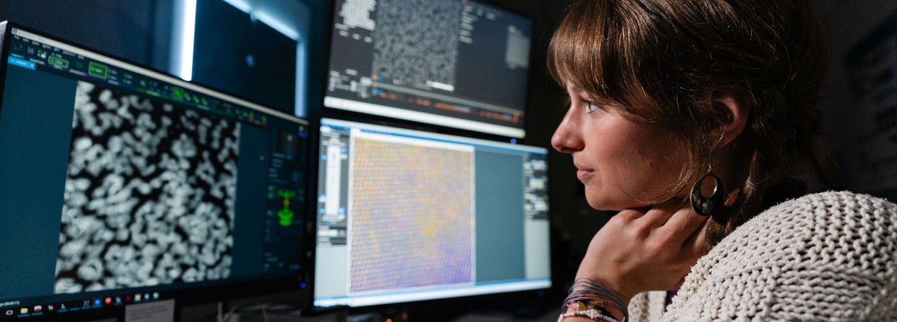 Person analyzing scientific data on multiple computer monitors in a research environment.