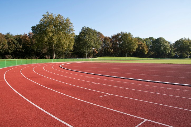 An empty running track with a field of grass and trees in the background