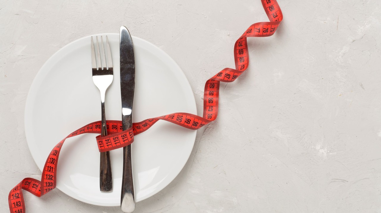 white dinner plate with a red tape measure and knife and fork 