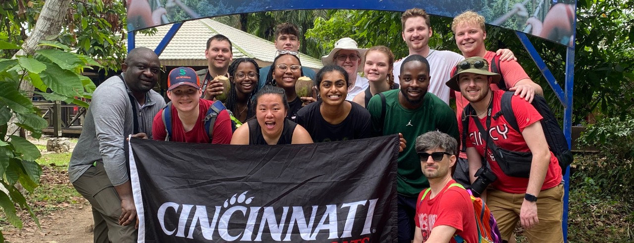 Cedrick Kwuimy and UC students hold up a Cincinnati Bearcats banner in Ghana.