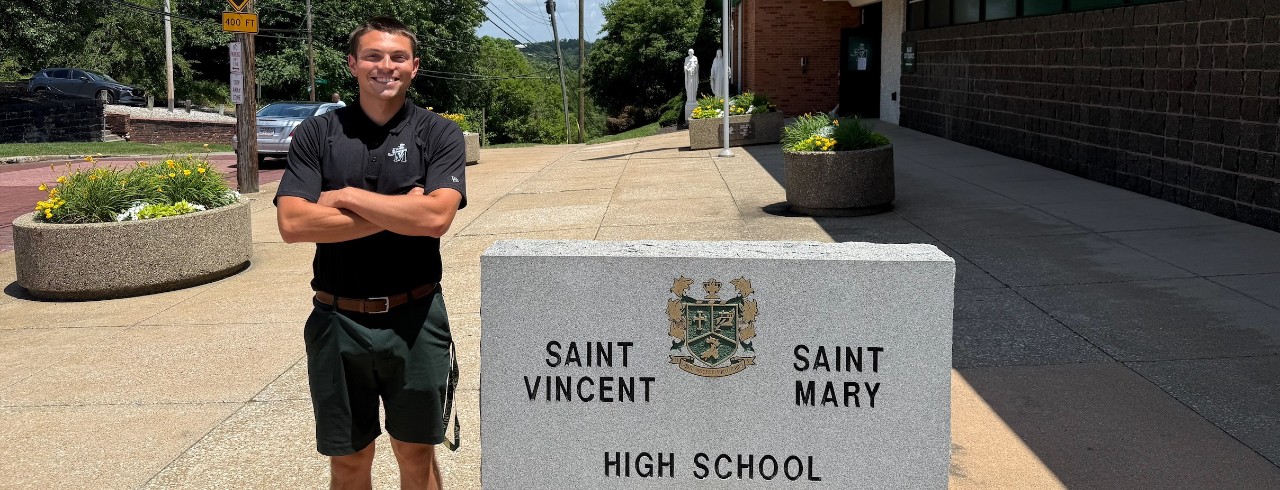 Thomas Matthew stanind in fron of the St. Vincent St. Mary sign at his new job