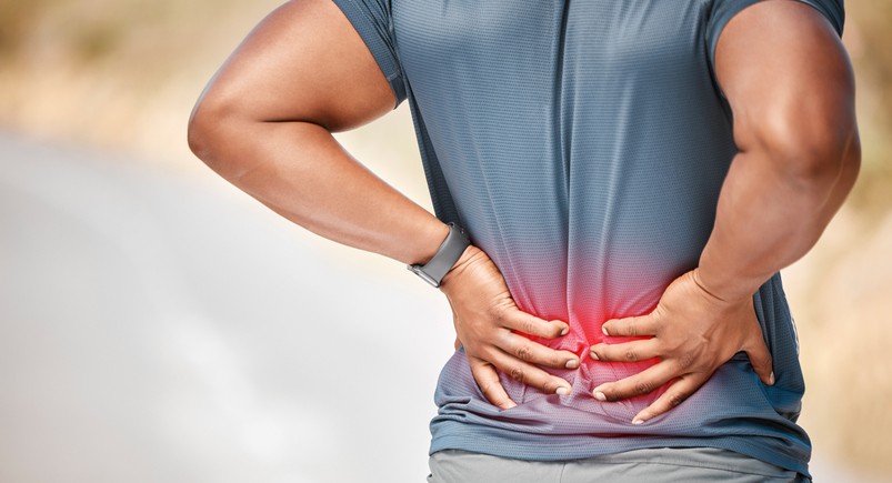 A person holding their lower back in pain with red illustration on the back highlighting where the pain is