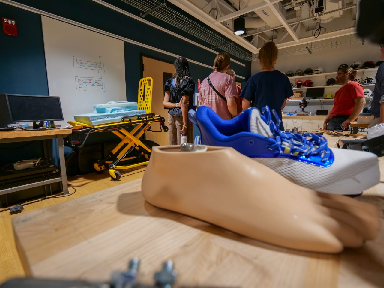 A closeup of a mannequin foot on a lab bench with high school students in the background.