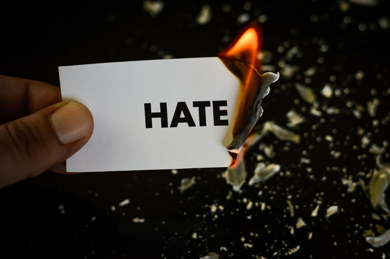 image of a hand holding a note that says hate which is buring