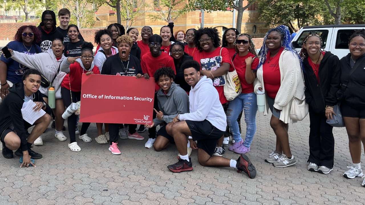 A group of UC students hold an Office of Information Security sign while posing for a photo with OIS staff