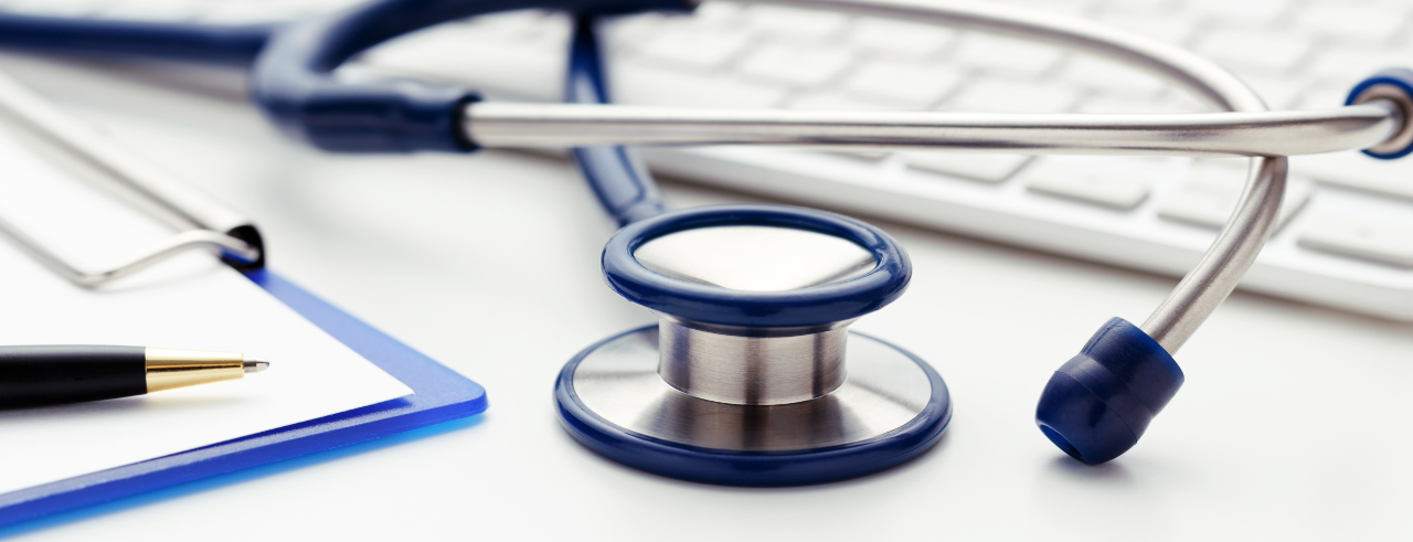 Stock photo featuring a stethoscope atop a keyboard, with a clipboard and pen in the corner of the photo