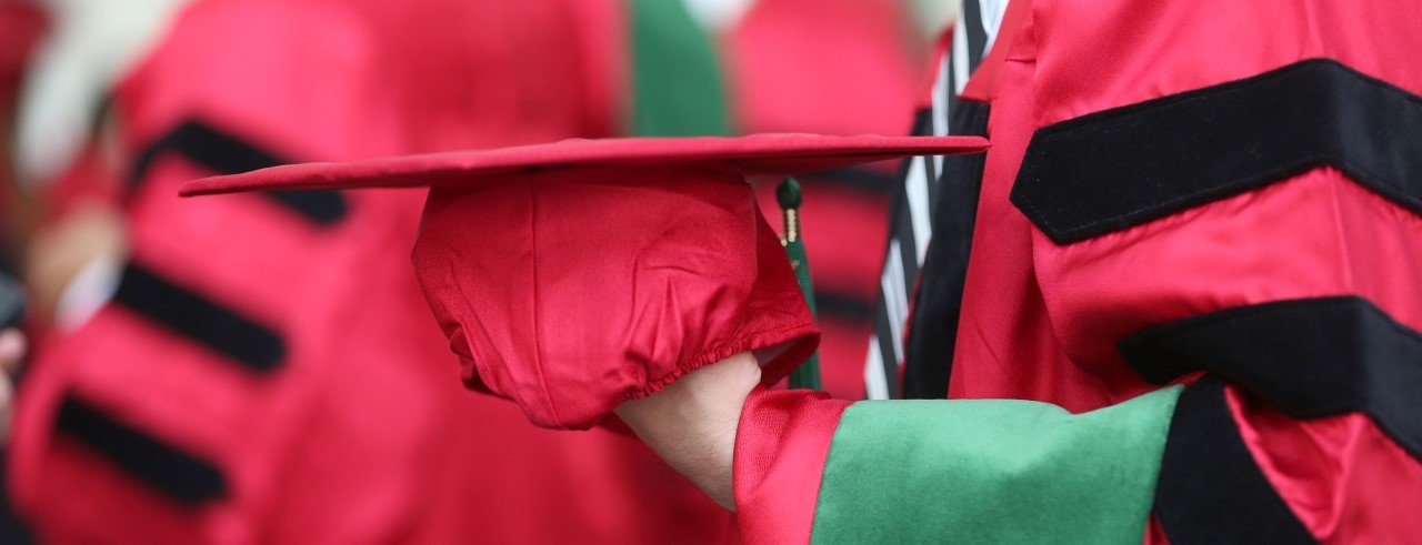 Close-up of a master's grad holding red cap and gown when finishing graduate school