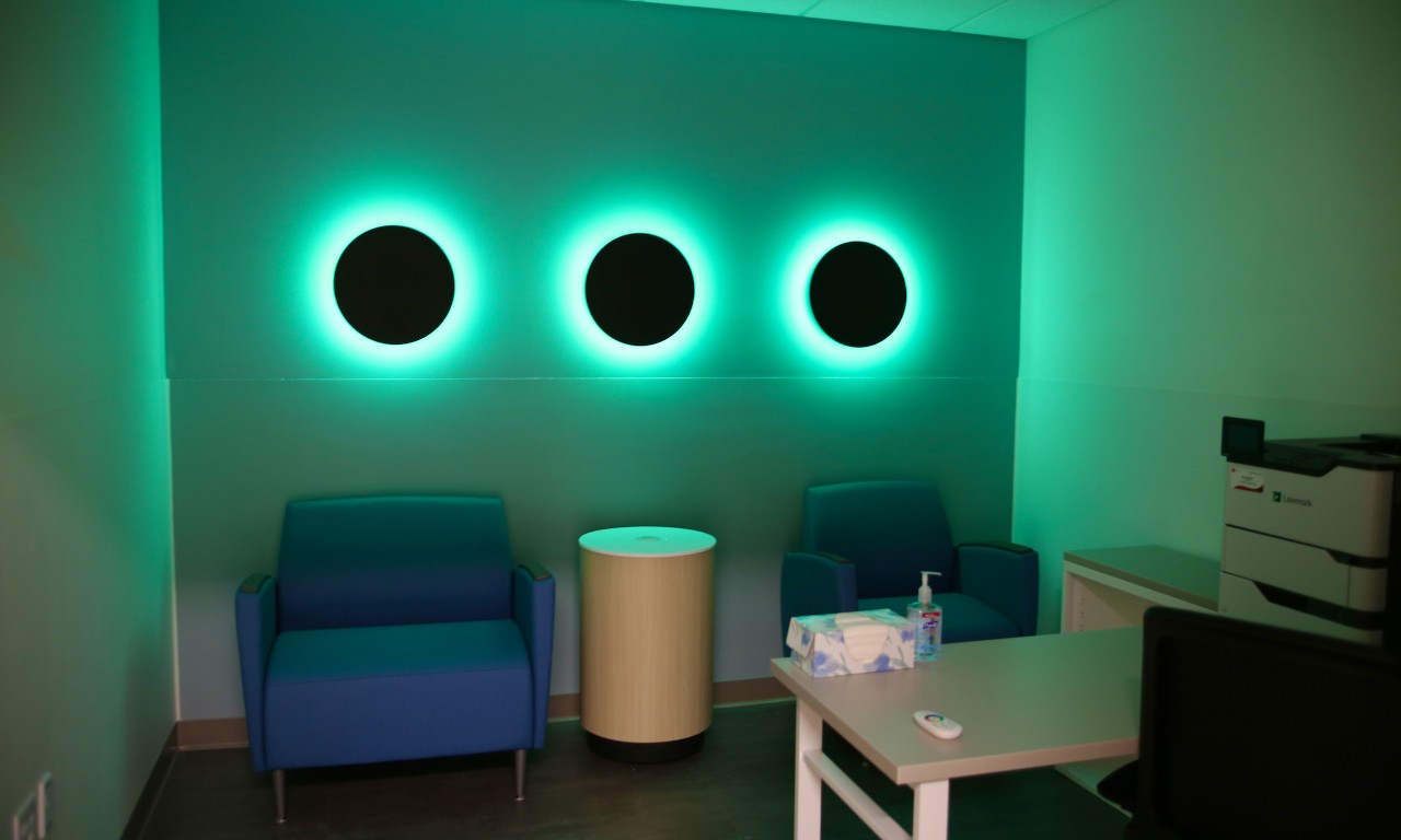A medical clinic room with bright neon green lighting emanating from three black dots on the wall.