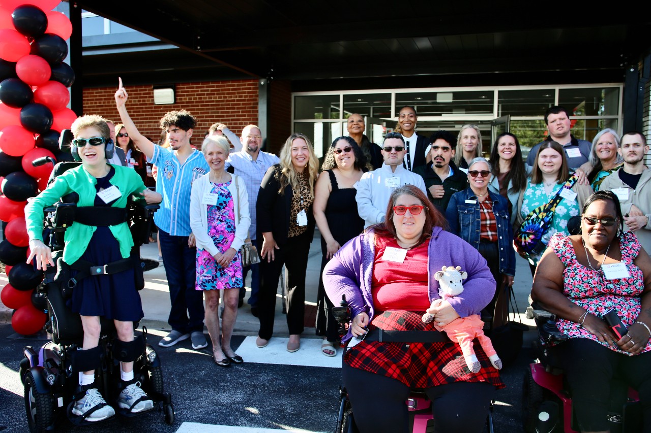 Several people stand beside a tower of red and black balloons in front of a new medical building.