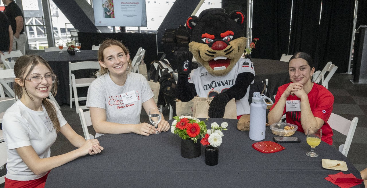 Three students sitting at a table with the UC Bearcat.